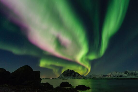 Green and pink Northern lights above the mountains and coast