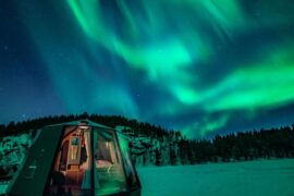 glass igloo in the snow under a sky of nothern lights