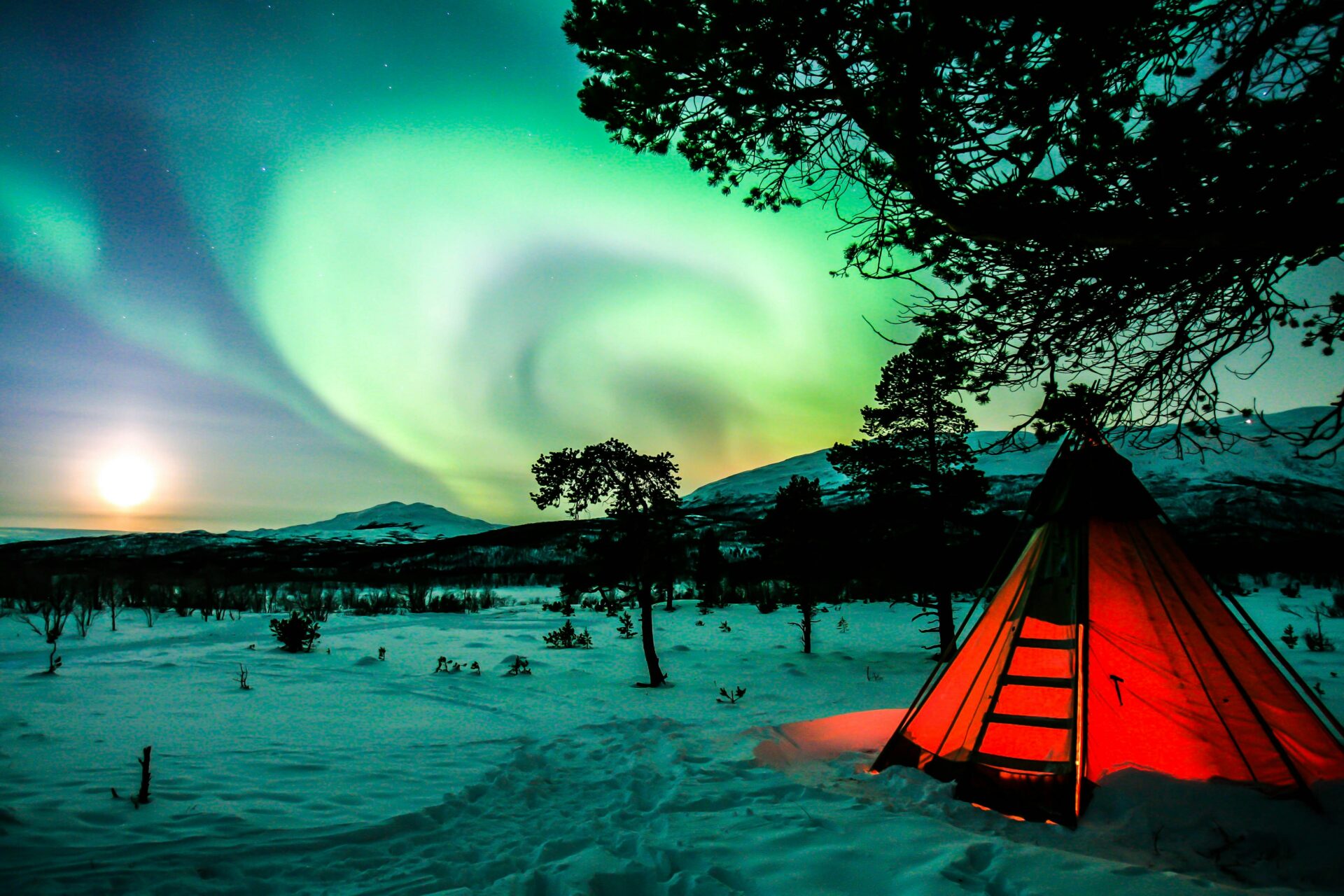 northern lights on a snowy landscape with lit up tent in one of the national parks in sweden