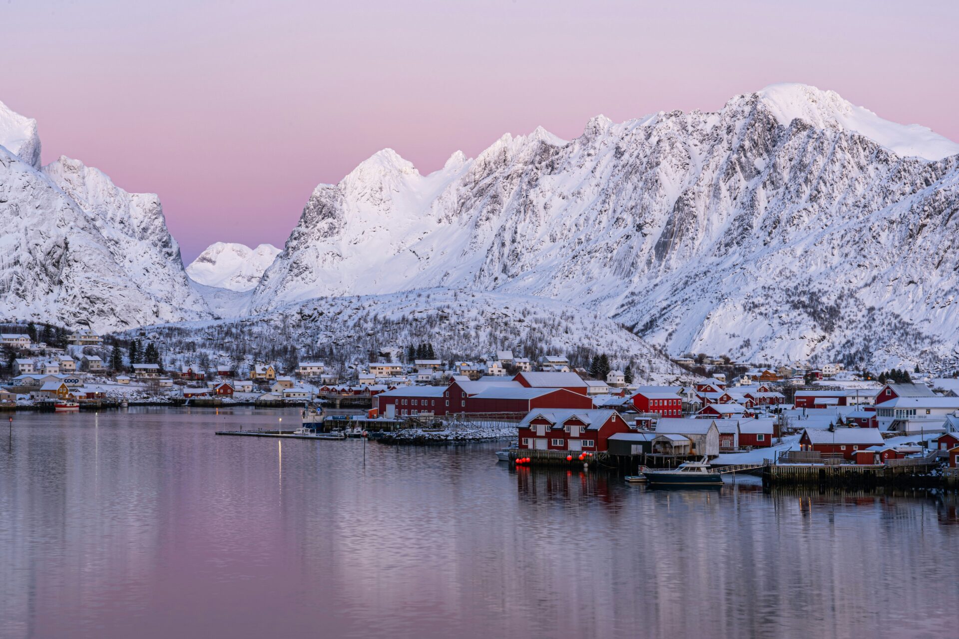 red cabins by the sea surrounded by mountains covered by snow 