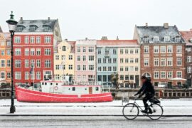 man riding on bicycle in front of colourful houses in copenhagen