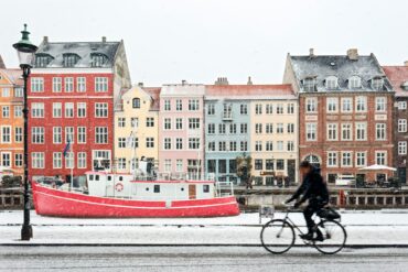 man riding on bicycle in front of colourful houses in copenhagen