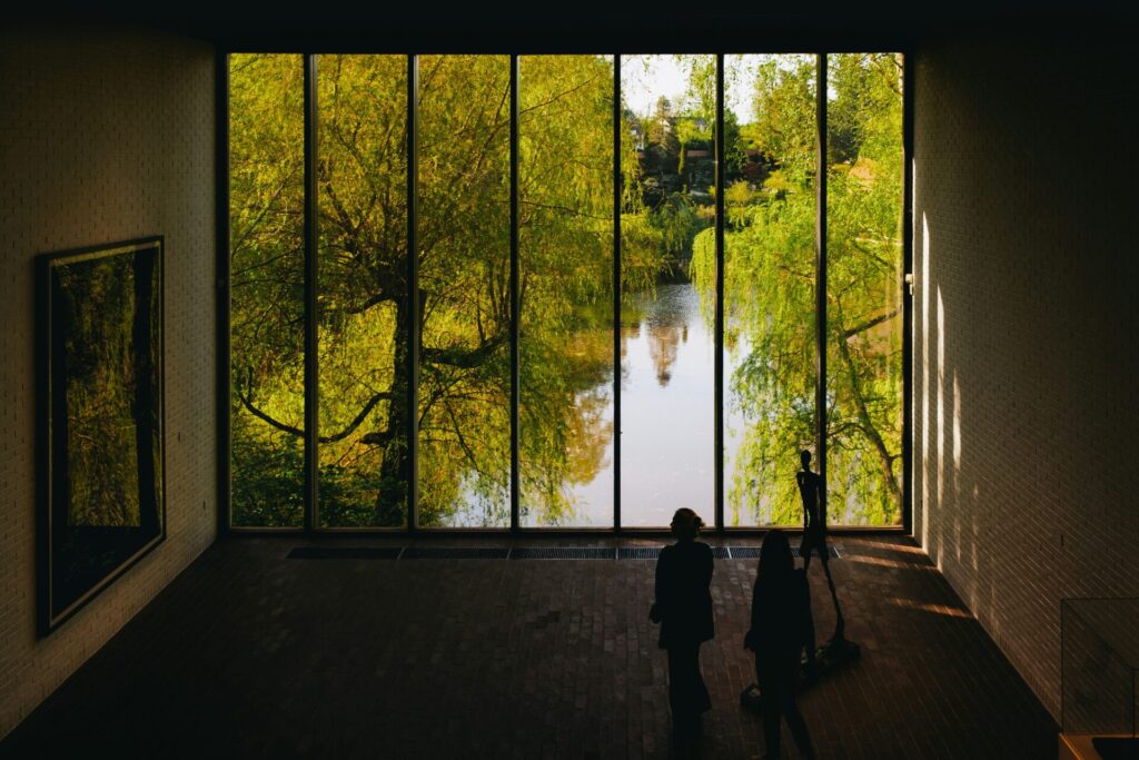 people standing in front of large window with trees and water