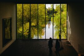 people standing in front of large window with trees and water