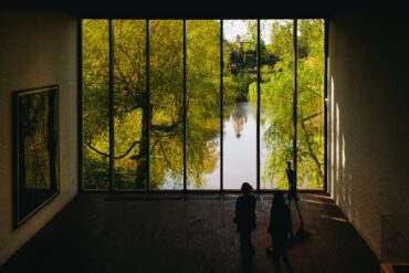 people standing in front of large window with trees and water